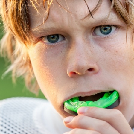 Young boy placing green athletic mouthguard in his mouth