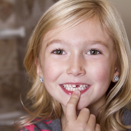 Girl with missing tooth pointing to her smile