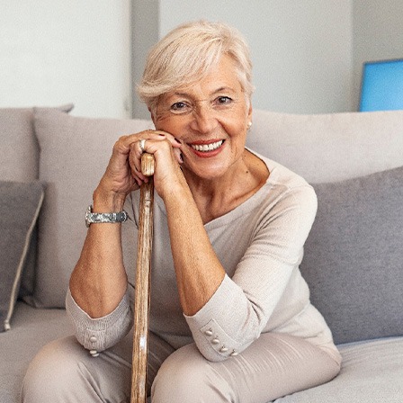 Woman in beige clothes on beige couch smiling and leaning on walking cane