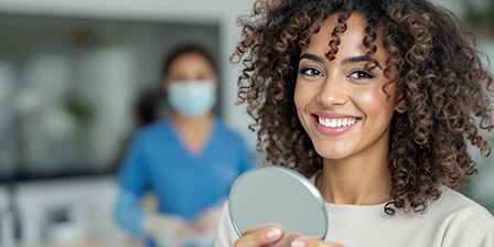 Woman smiling while holding small mirror in dental office