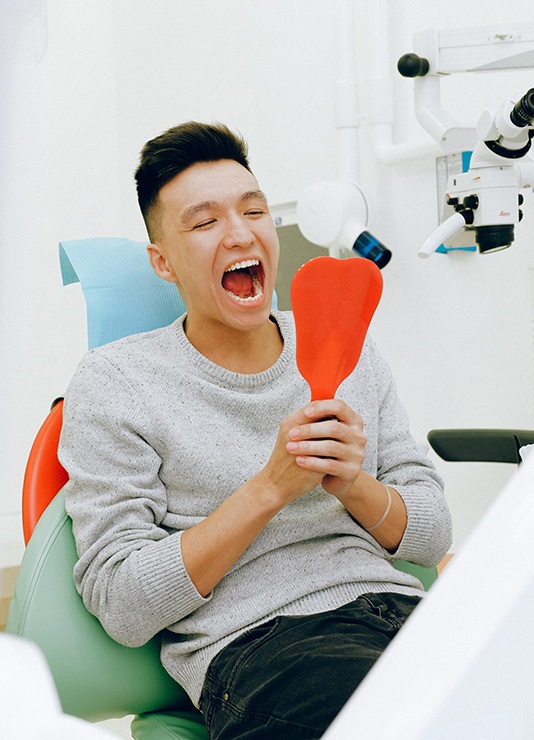 Man in dentist’s chair looking at mouth in mirror
