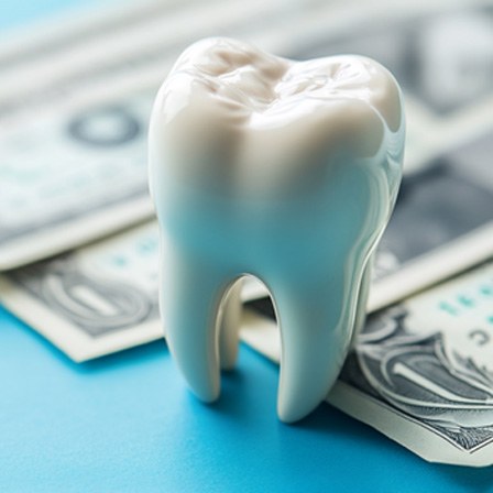 Large model tooth next to dollar bills on light blue surface.