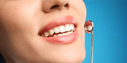 Nose-to-neck ¾ profile of woman smiling next to dental mirror