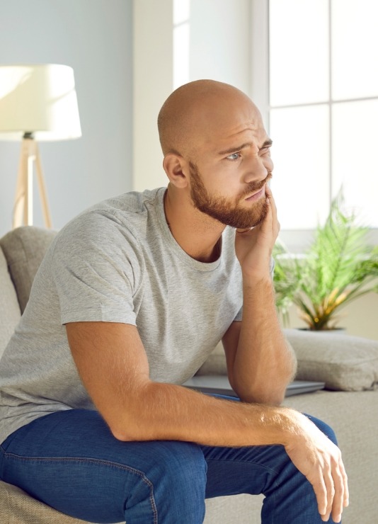 Man sitting on couch and holding his cheek