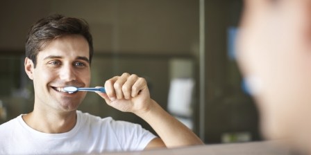 Man smiling while brushing his teeth