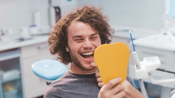 Man admiring his smile in mirror after dental services in Oklahoma City