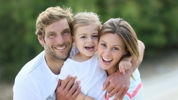 Family of three grinning outdoors