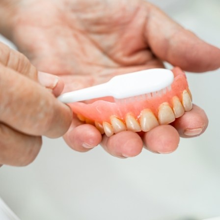 Person cleaning their denture with a toothbrush