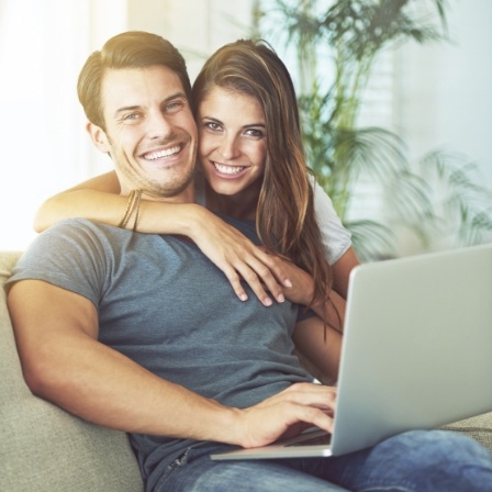 Man with laptop sitting on couch smiling with woman