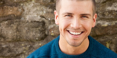 Man in blue shirt standing in front of a stone wall