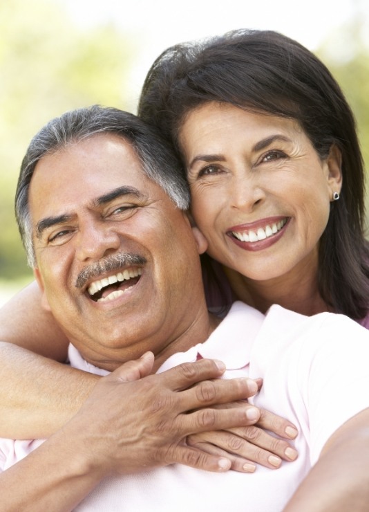 Man and woman smiling outdoors with implant dentures in Oklahoma City