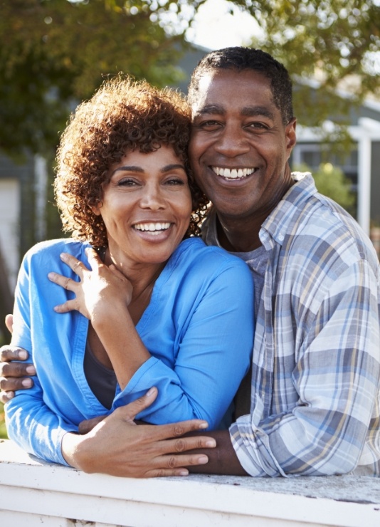 Man and woman smiling in their front yard after replacing missing teeth