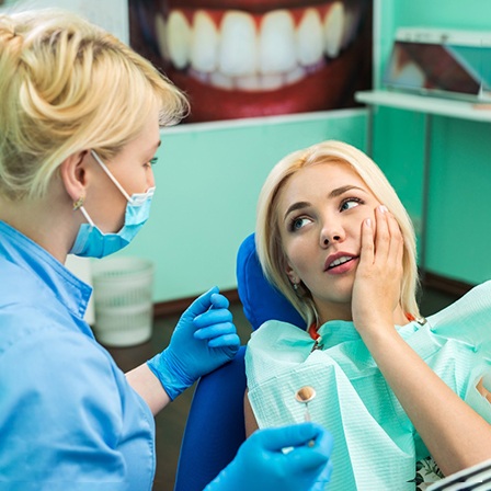 Woman in dental chair holding her cheek in pain