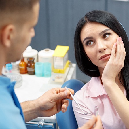 Woman holding her cheek in pain while sitting in dental chair