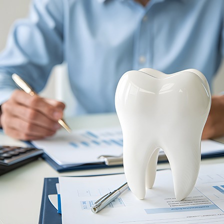 Man in blue shirt at desk with papers, pen, calculator, and large model tooth