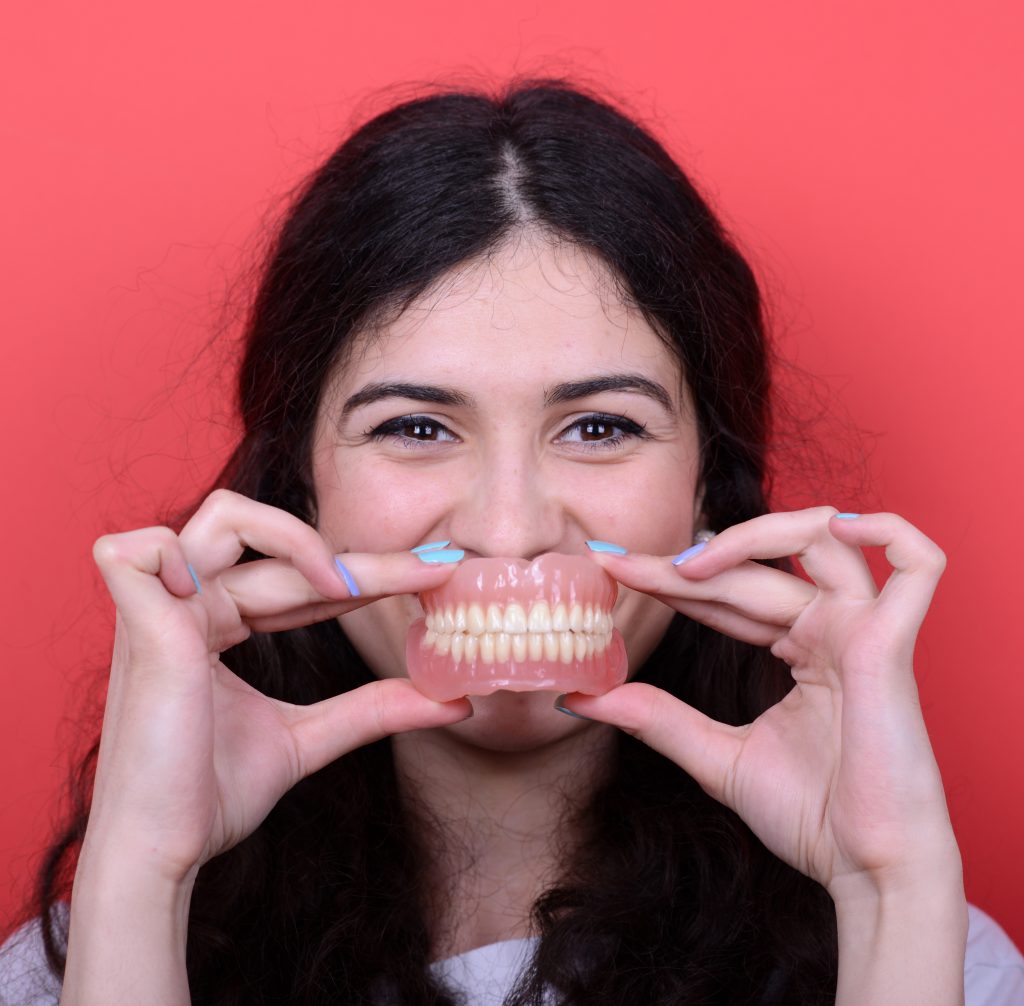 Portrait of happy woman with healthy smile holding denture again OK