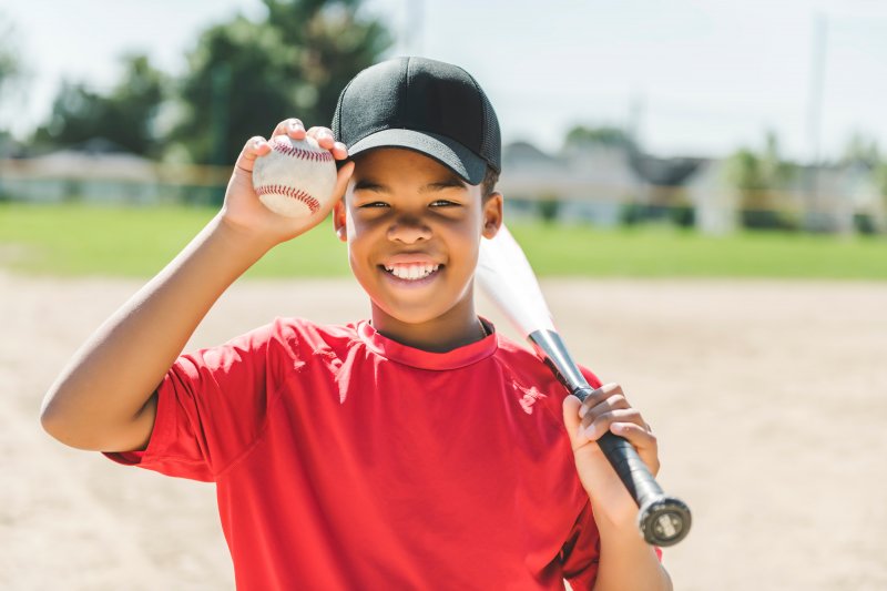 Kid smiles holding baseball and bat.
