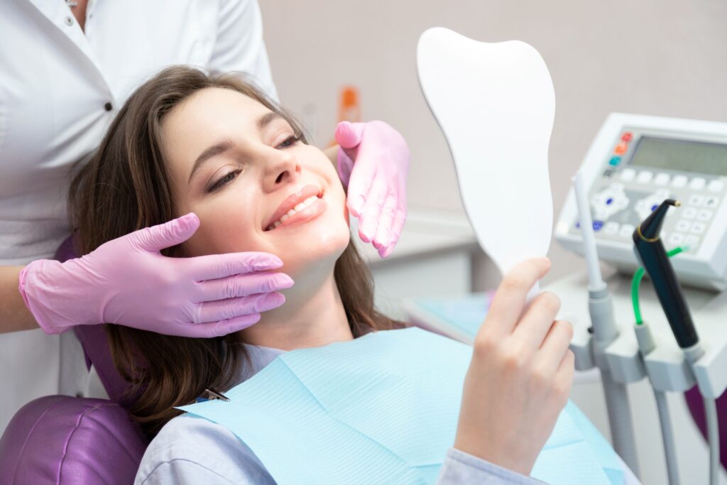 Woman with short hair in dental chair smiling at her reflection in mirror