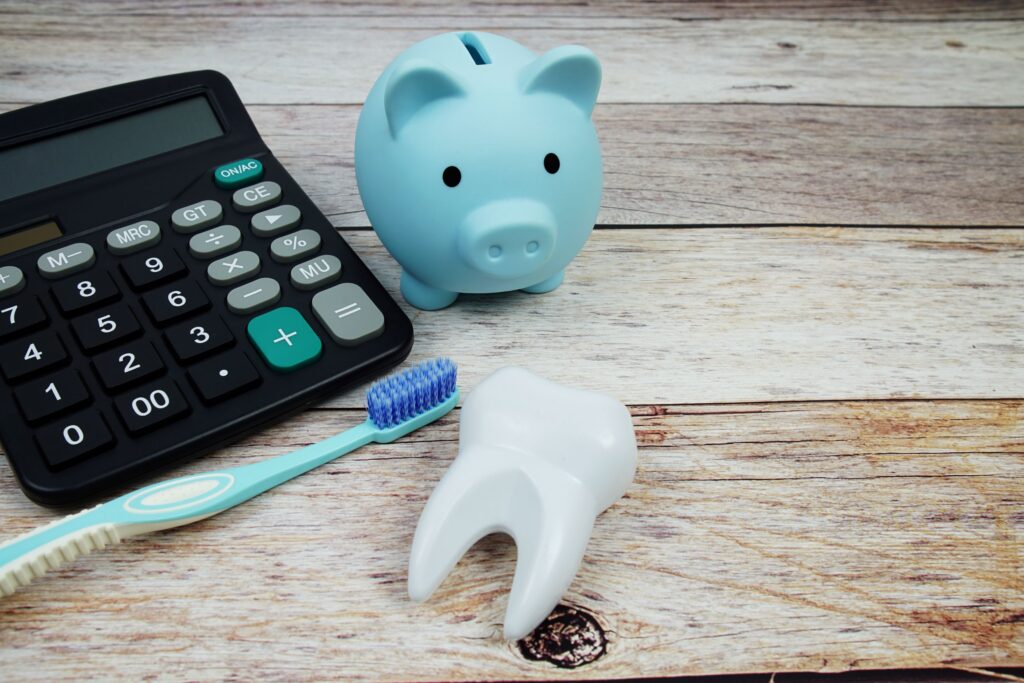 Blue piggy bank, calculator, toothbrush, and model tooth on wooden surface