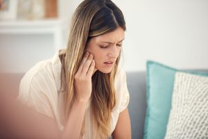 Woman on couch with eyes closed touching fingers to jaw in pain